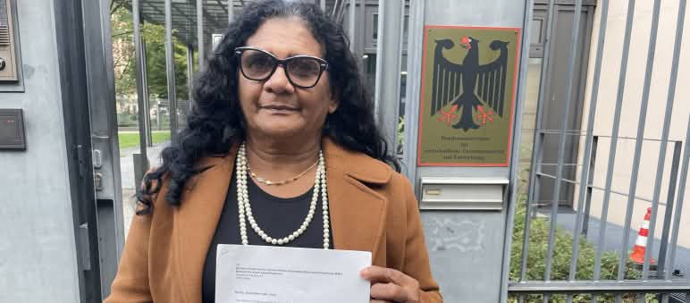 Quilombola woman Marli Borges holding a letter outside the barred entrance to the Federal Ministry for Economic Cooperation and Development (BMZ)