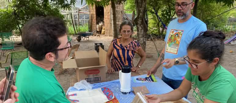 Two women display notebooks spread out on a table, made from the leaves of banana trees