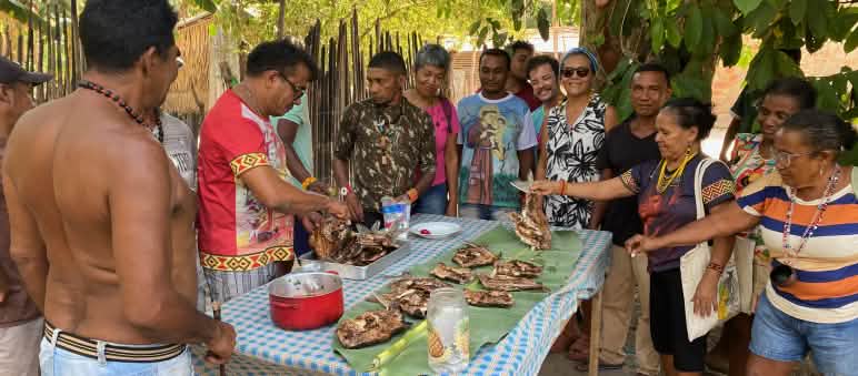 A group of 12 Indigenous people surround a table with grilled fish