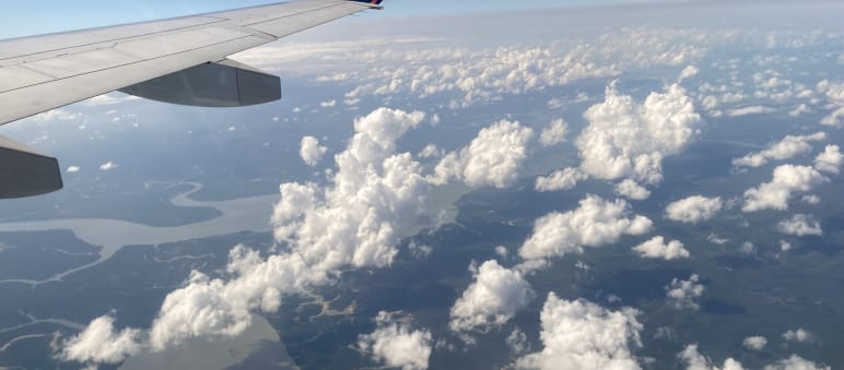 "Sustainable" air travel with carbon credits from offsetting projects in the rainforest? View of clouds, rivers and rainforest seen from an airliner, with the wing at the top of the frame