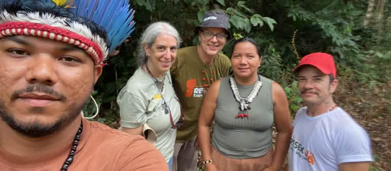 Selfie of an Indigenous person wearing a feather headdress on the left, with four people behind him in front of rainforest vegetation