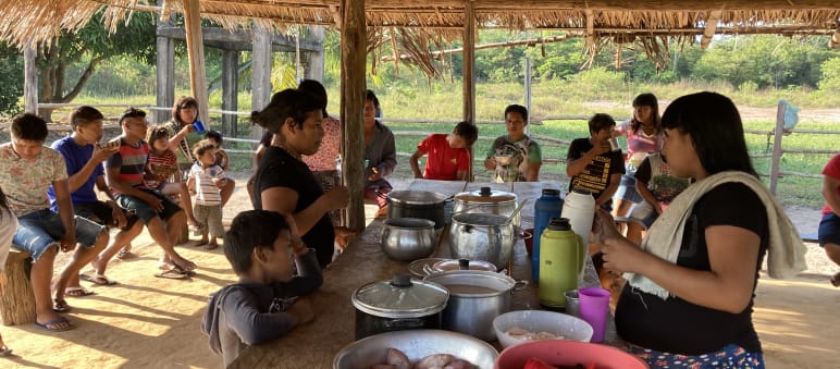 Indigenous women, children and young people eating together in an open hut