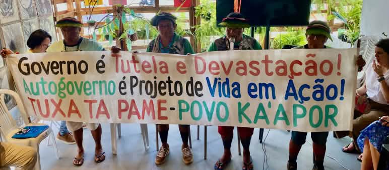Four Indigenous Kaápor hold up a banner with writing on it in a meeting room