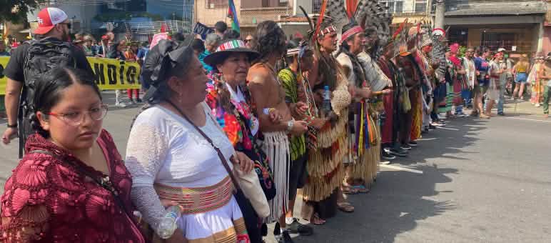 Indigenous women and men dressed in colorful clothing form a line at a demonstration
