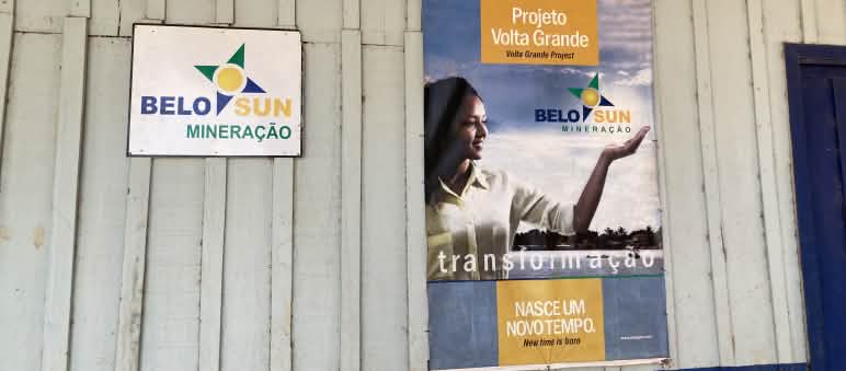 A sign for the mining company Belo Sun and a poster with company propaganda on the wall of a wooden hut