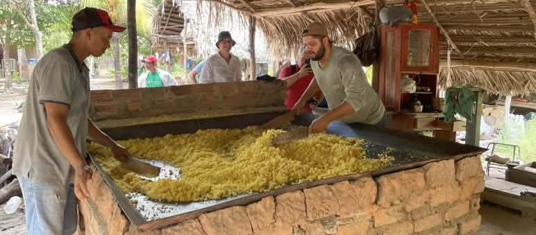 Two men roast cassava in a large square metal pan