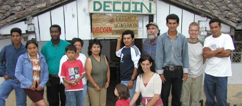 Group of people from DECOIN and Rainforest Rescue in front of a wooden hut with the inscription DECOIN
