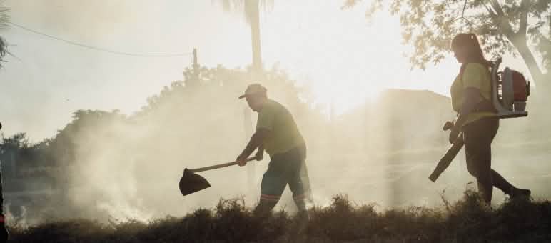 A man with a fire beater and a woman with a portable blower during an exercise, backlit