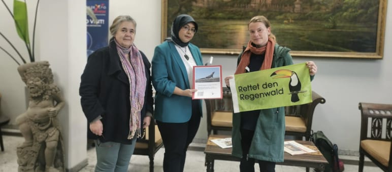 Three women with Rainforest Rescue banner in front of temple painting