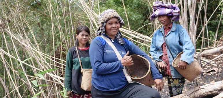 Three Dayak women with collecting baskets smile at the camera.