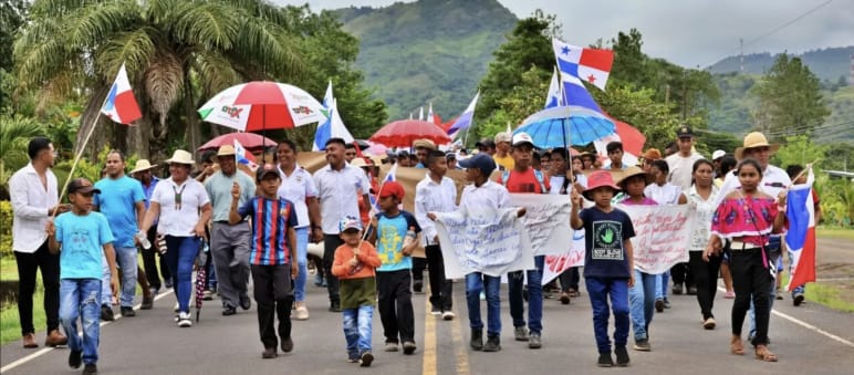Protesters march with banners, national flags and umbrellas on a country road in Panama