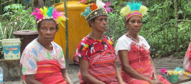 Three women dressed in red fabric and colorful feather headdresses