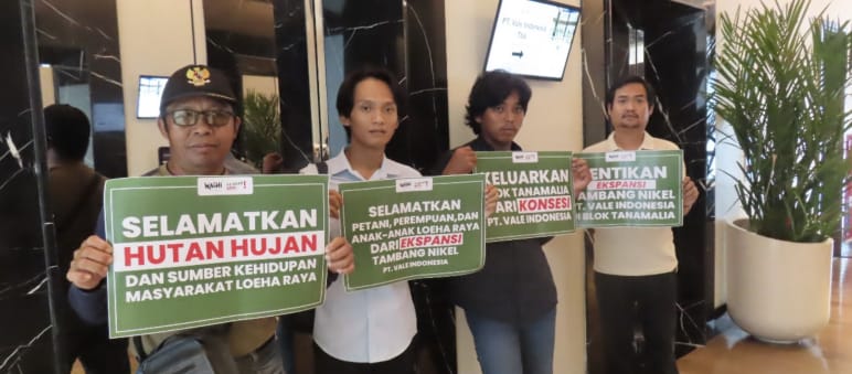Four men hold placards reading “Save the forest and livelihoods of the people of Loeha Raya”