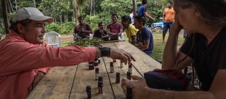 Two men discuss small bottles of essential oils arranged on a table