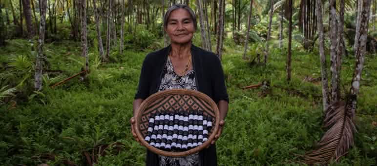 An Indigenous woman in the rainforest presents a basket filled with small bottles of essential oils
