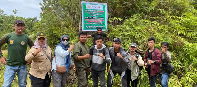 A group of people standing in front of a warning sign stating that any activity in the forest is subject to heavy fines