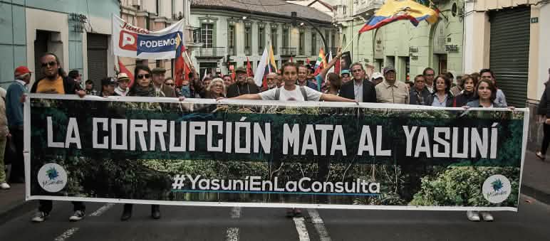 A protest march moves down a street carrying a large banner