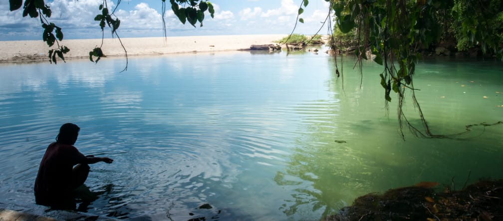Sulawesi has 6,000 kilometers of coastline, with sandy beaches, steep slopes and quiet bays. A woman is sitting in the water in a bay lined with rocks and a sandy beach