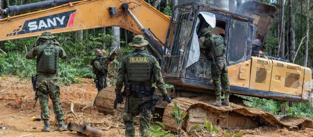 A group of men in camouflage suits from the environmental agency IBAMA disables a yellow excavator in the rainforest