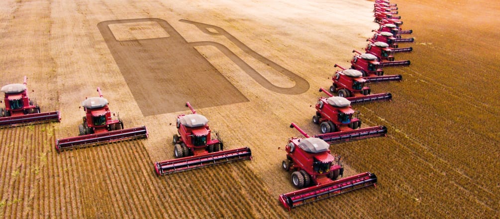 Photomontage: 15 combines in a wedge formation harvesting a soybean plantation. The outline of a gas pump can be seen in the harvested area.