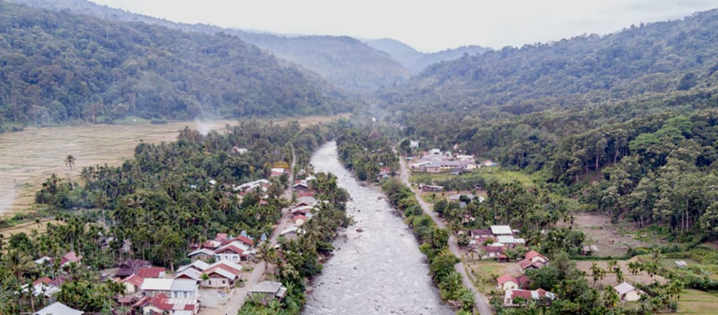 River flowing through a village, mountains in the background