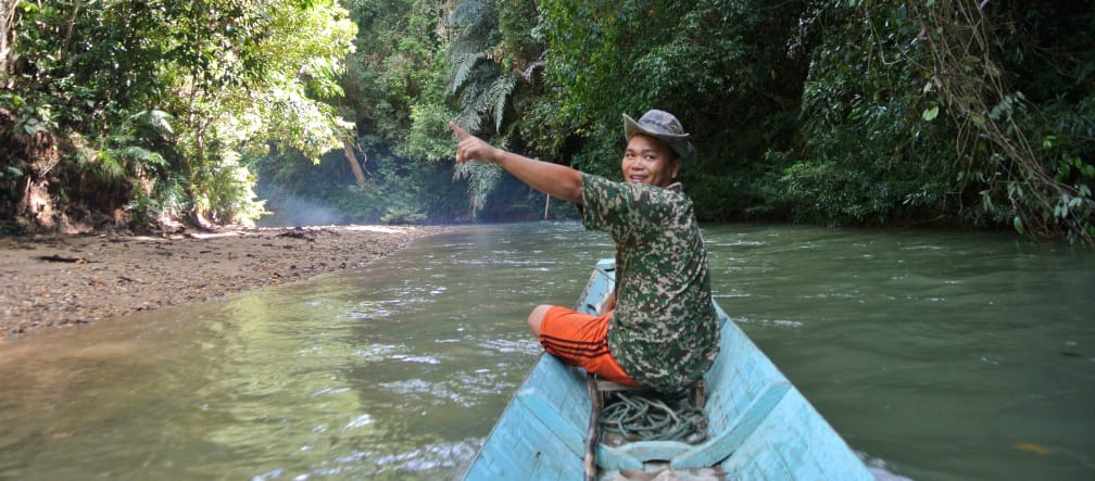 The indigenous Iban people are front-line defenders of forests and rivers A smiling man at the helm of a small boat points toward the rainforest