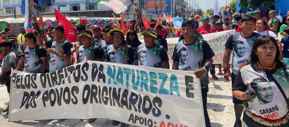 A group of around 15 Indigenous people with feather headdresses and a large banner