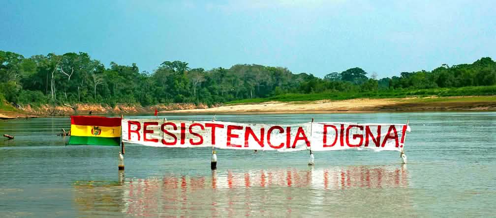 Protest banner on a river in the Bolivian rainforest: the slogan “Resistance Means Dignity” stands next to the Bolivian flag.