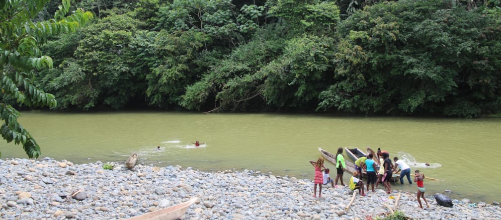 People and canoes on the bank of a river in the rainforest and children swimming