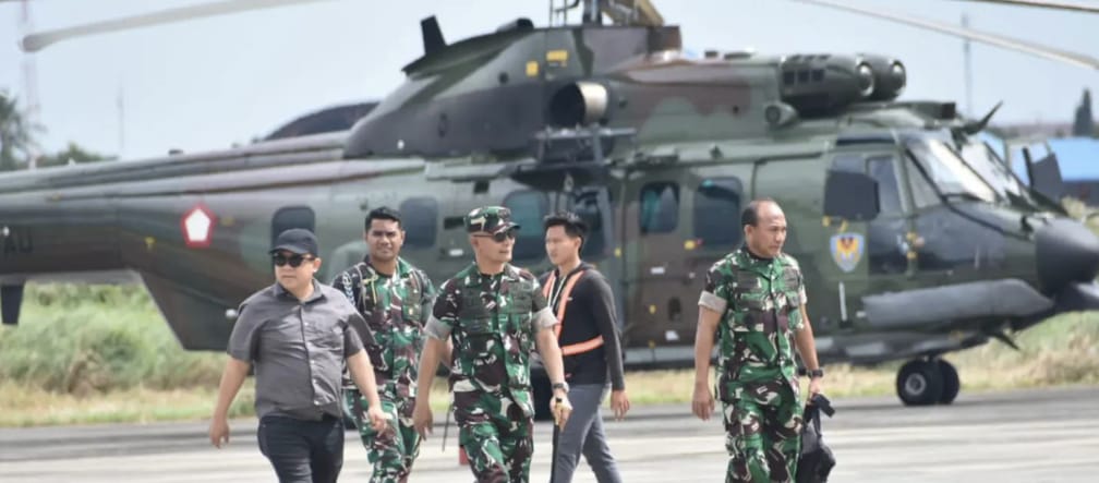 Three soldiers and two civilians walking in front of a helicopter