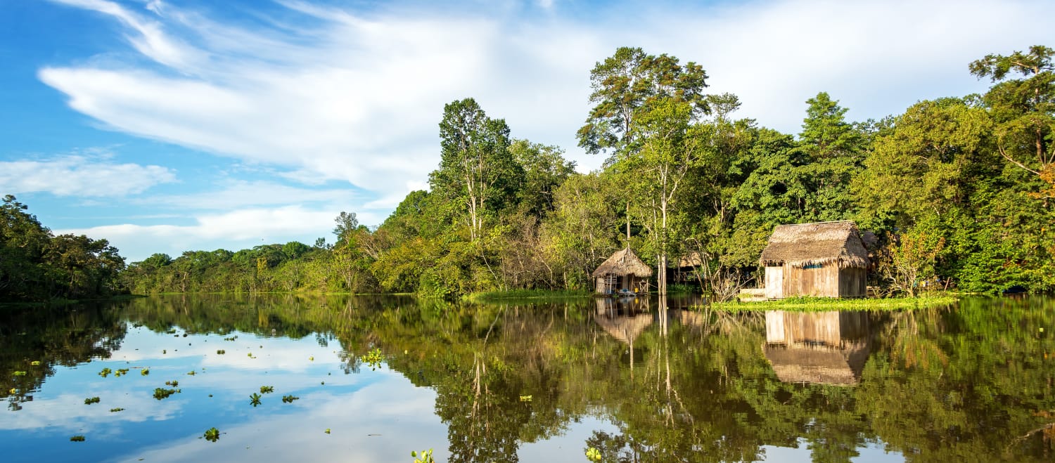 The Amazon rainforest and a wooden hut are reflected in the waters of the Yanayacu River in Peru