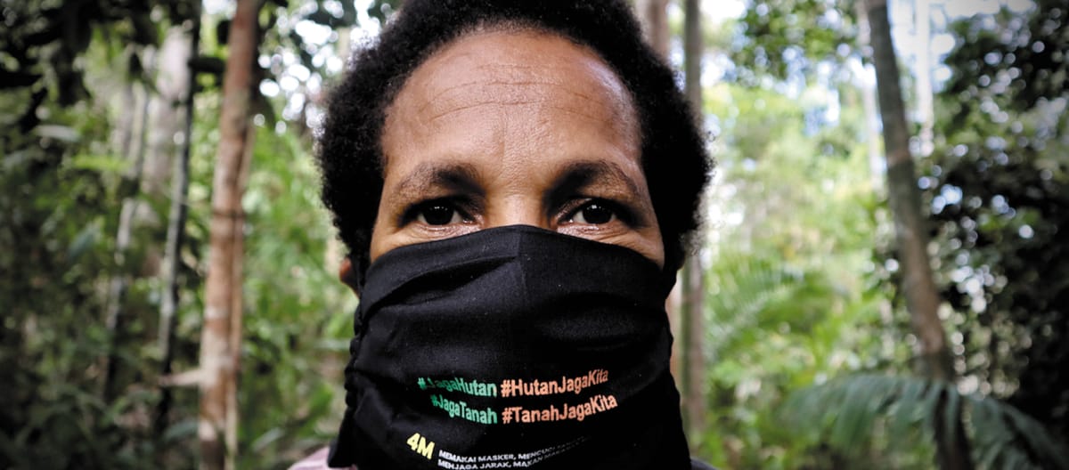 Papuan woman wearing a mask with the slogan “Protect the forest – the forest protects us”