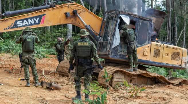 A group of men in camouflage suits from the environmental agency IBAMA disables a yellow excavator in the rainforest
