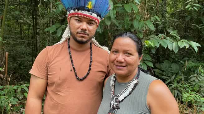 Portrait of an Indigenous woman wearing a feather necklace on the right and a young Indigenous man wearing a feather headdress on the left