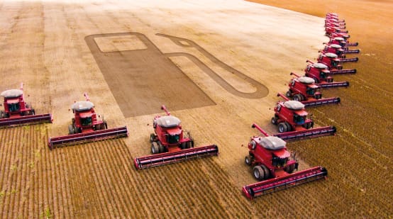 Photomontage: 15 combines in a wedge formation harvesting a soybean plantation. The outline of a gas pump can be seen in the harvested area.