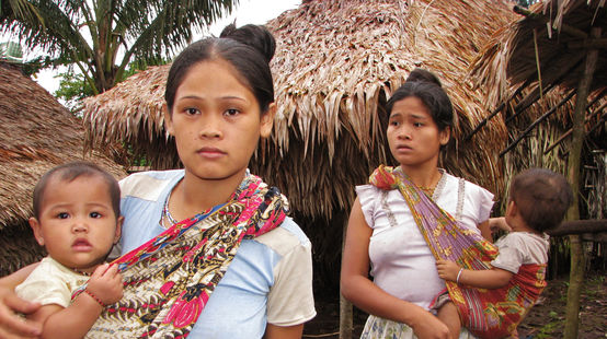 Two women with their children in front of thatched houses