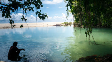 A woman is sitting in the water in a bay lined with rocks and a sandy beach