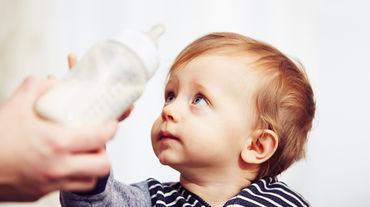 A worried-looking baby pushing its bottle away