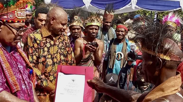 Presenting the certificate of recognition for the Indigenous community and ancestral forest A group of Papuans in traditional clothing holding a certificate