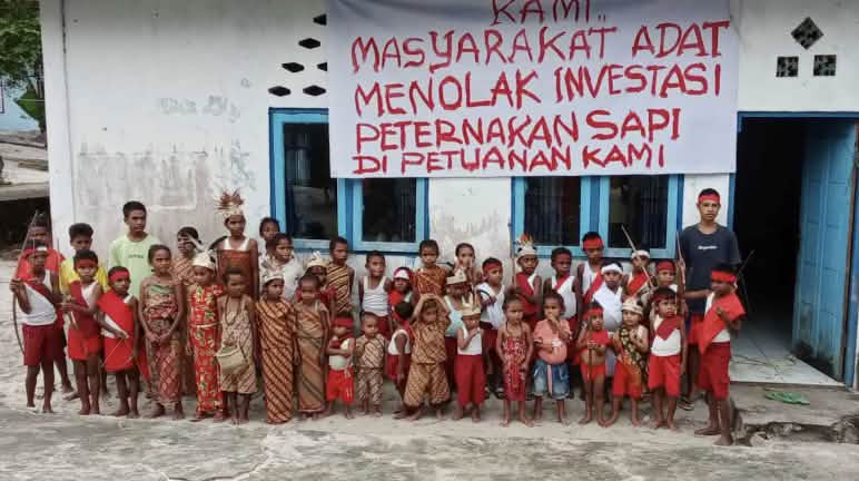 “We Indigenous people reject investment in cattle ranching on our land!” Children in front of a school and a banner reading “We Indigenous people reject investment in cattle ranching on our Indigenous land”