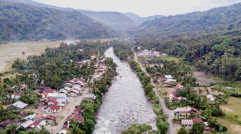River flowing through a village, mountains in the background