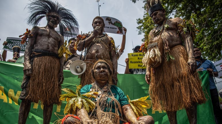 Four Indigenous Papuans in traditional clothing in front of banner