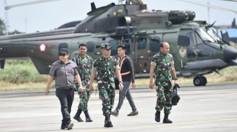 Three soldiers and two civilians walking in front of a helicopter