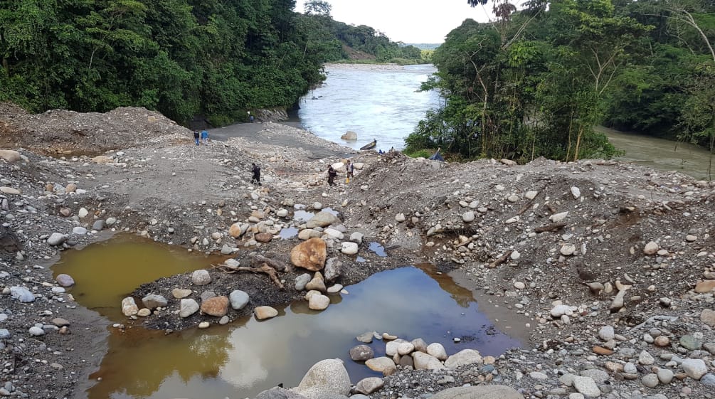 Excavated sediment and contaminated pools on a riverbank in the forest