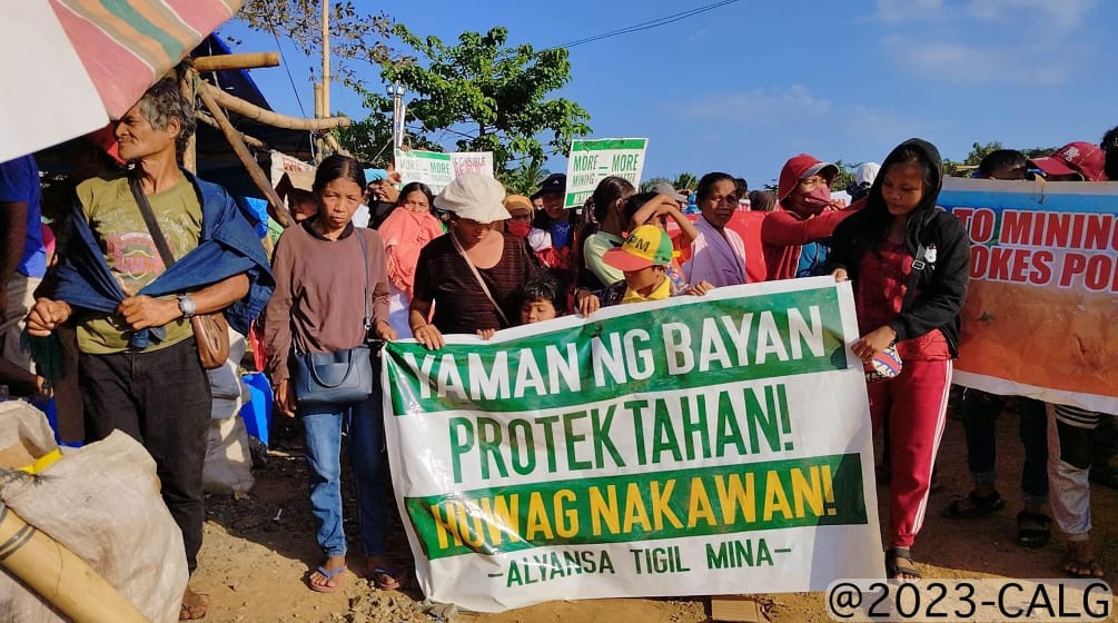 A group of people holding a banner that reads (translated): “Protect the wealth of the people! Stop the theft! Alliance Against Mining”