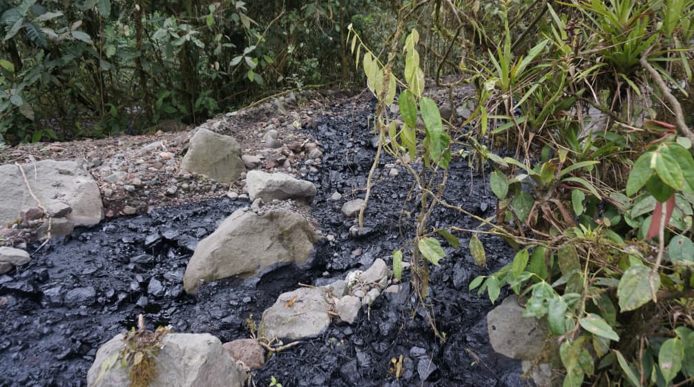 A stream of black crude oil has spilled over an area covered with gravel and stones