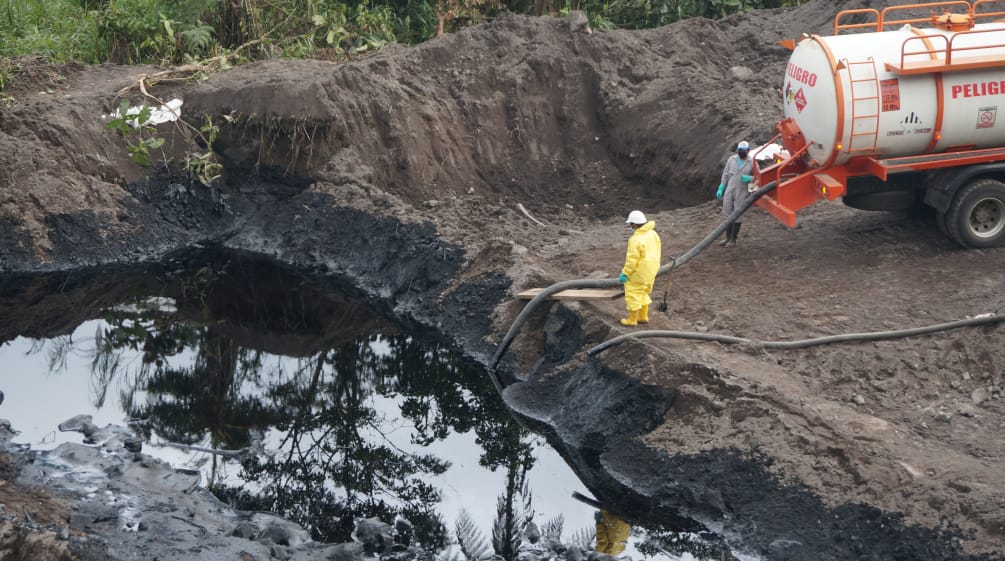 Two oil workers use a hose to suck crude oil from an earthen pond into a tanker truck