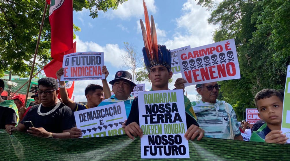 Indigenous people marching in a row holding up placards with slogans such as: “Our land is our future”