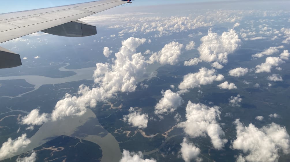 View of clouds, rivers and rainforest seen from an airliner, with the wing at the top of the frame