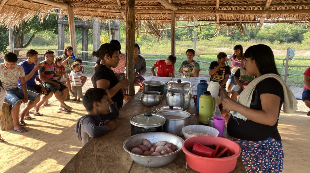 Indigenous women, children and young people eating together in an open hut